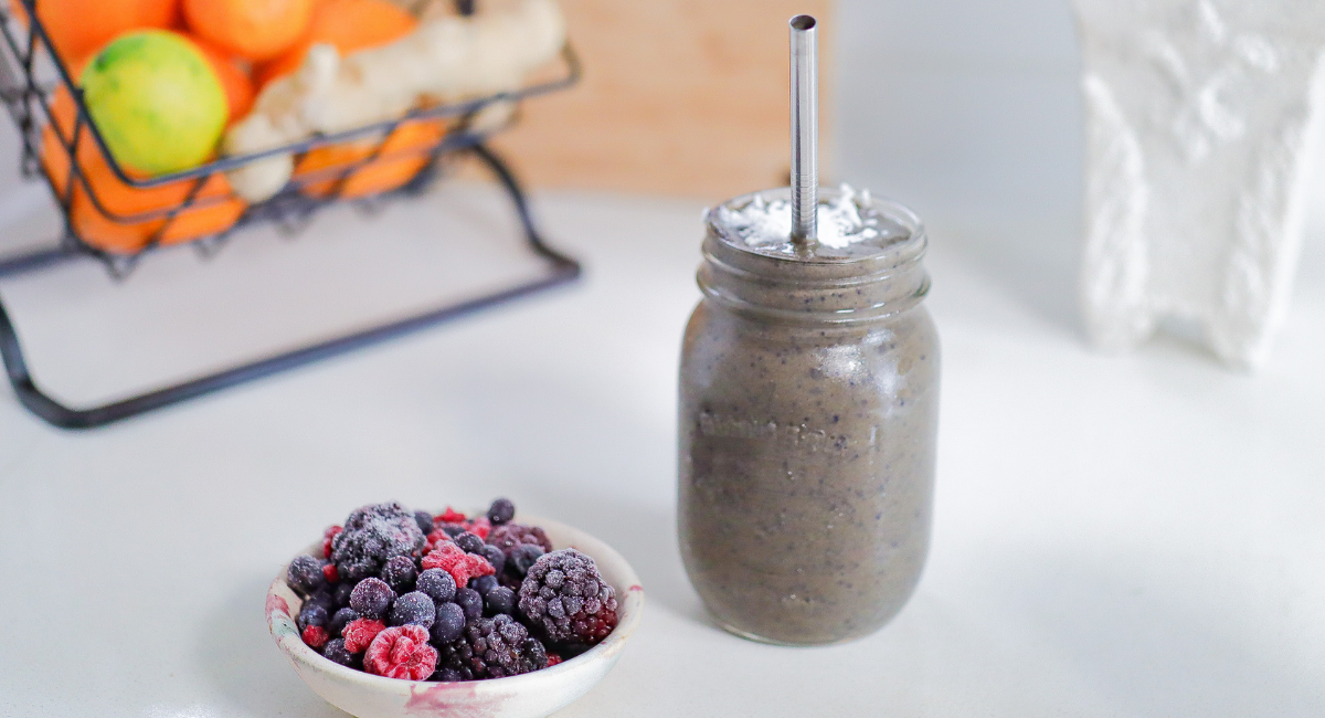 Smoothie in a jar next to bowl of berries on white counter