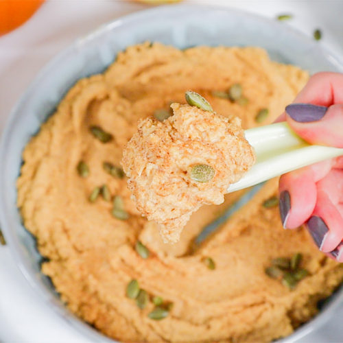 hand holding celery stick with hummus on it.