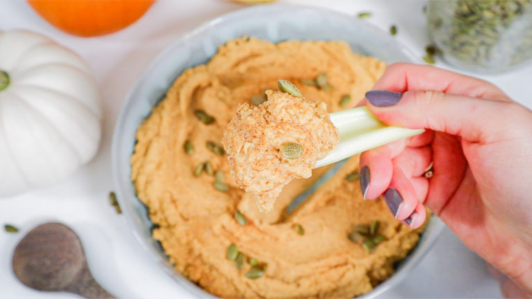 hand holding celery stick with hummus on it.