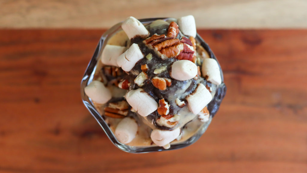 A sundae cup with chocolate ice cream topped with pecans and marshmallows