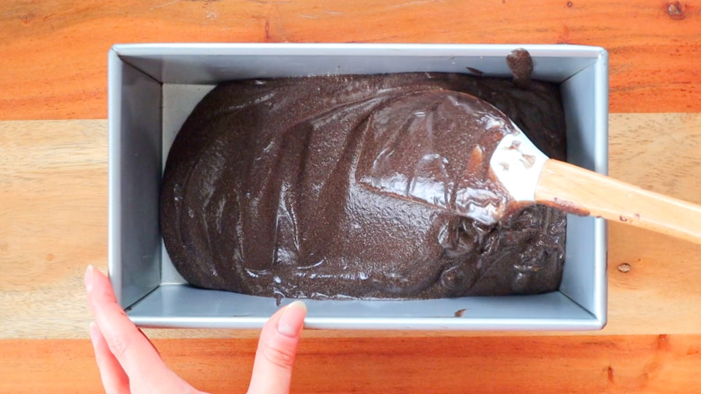 Liquid chocolate ice cream ingredients being smoothed into an even layer with a spatula in a tin