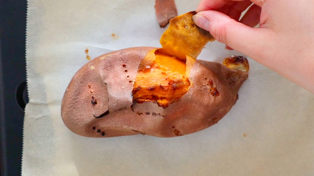 Fingers peeling the skin off of a baked sweet potato