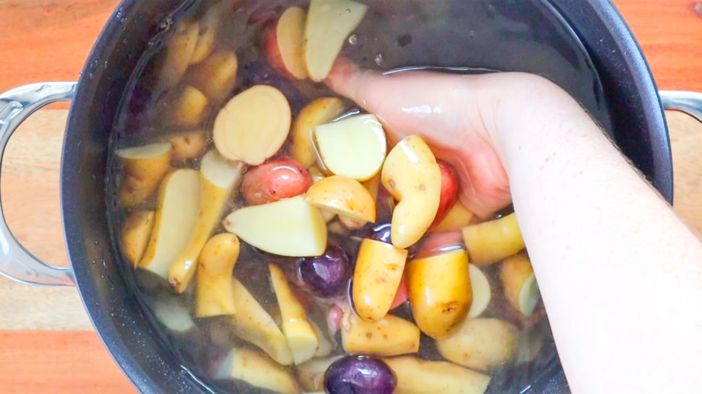 Hand holding cut potatoes in a pot of water