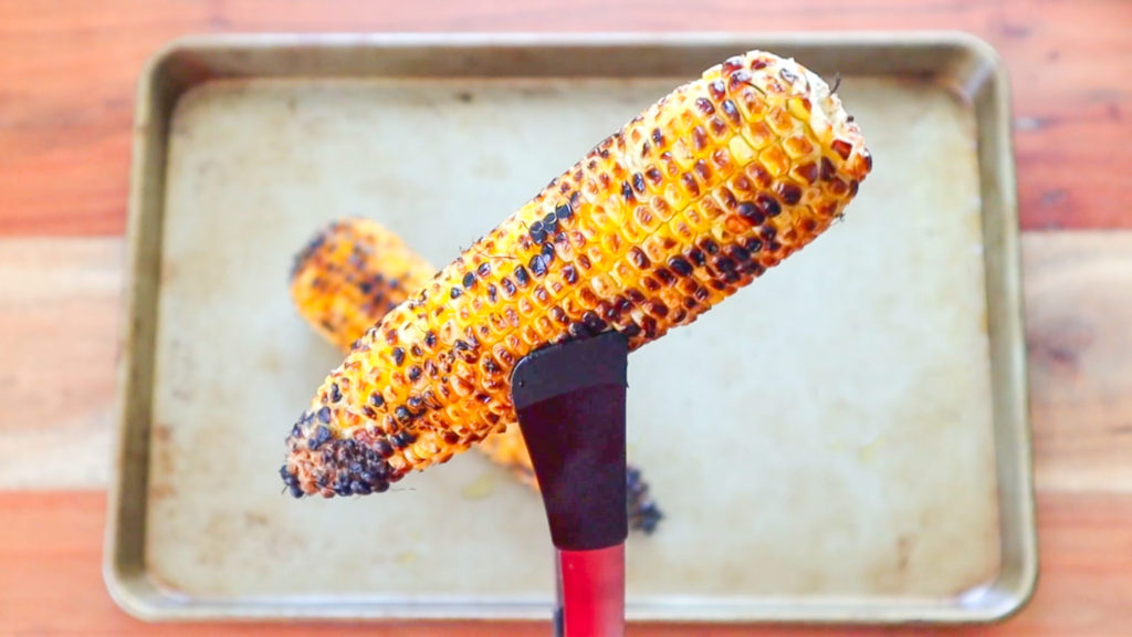 Tongs holding a grilled cob of corn