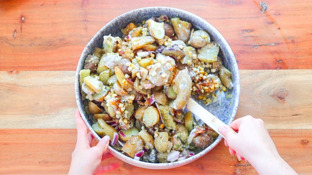 Hand stirring ingredients in a large bowl to make BBQ Ranch Potato Salad