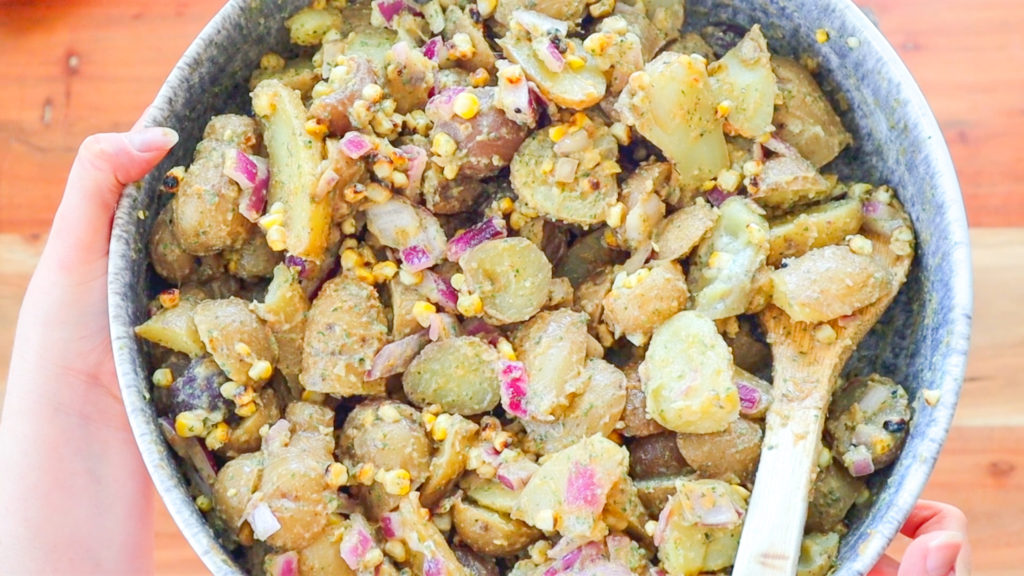 Close up image of BBQ Ranch Potato Salad, featuring potato pieces, corn, green onion, red onion, herbs