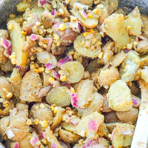 Close up image of BBQ Ranch Potato Salad, featuring potatoes, corn, green onion, red onion, herbs