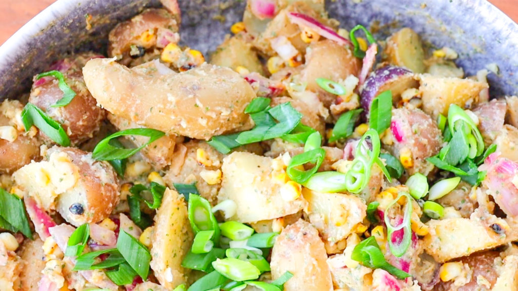 Close up image of BBQ Ranch Potato Salad, featuring potato pieces, corn, green onion, red onion, herbs