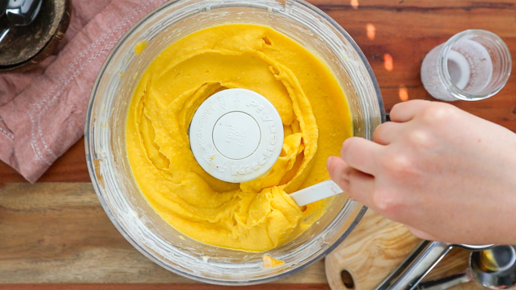 Hand scooping mango sorbet in a food processor