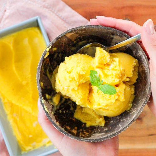 Hand holding a bowl of mango sorbet