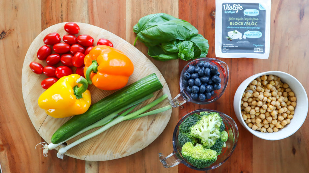 Ingredients on a wood table. Veggies, plant-based feta cheese, chickpeas.