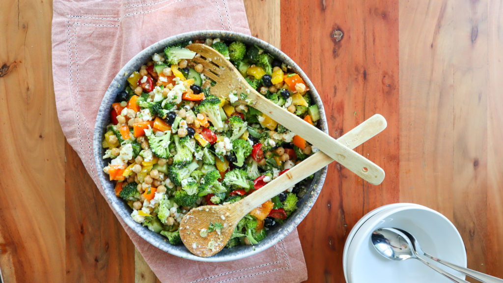 Serving bowl on a wood table, inside the bowl is Feta & Chickpea Rainbow Salad