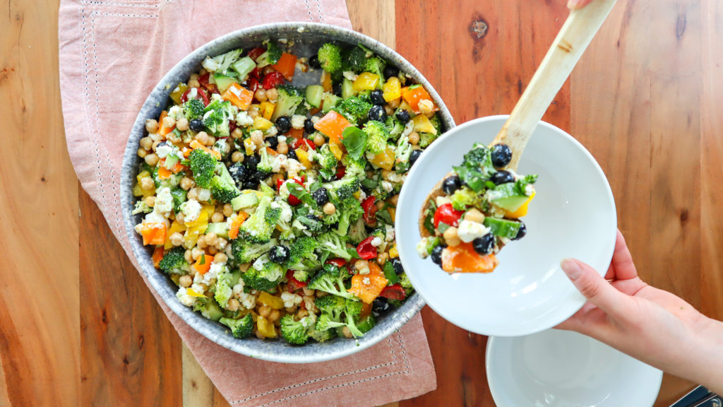 Hands holding a bowl and dishing out Feta & Chickpea Rainbow Salad