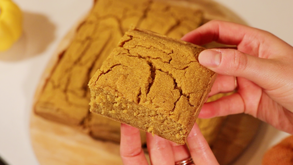 hands holding a slice of pumpkin cornbread, showing the crackled texture of the top of it