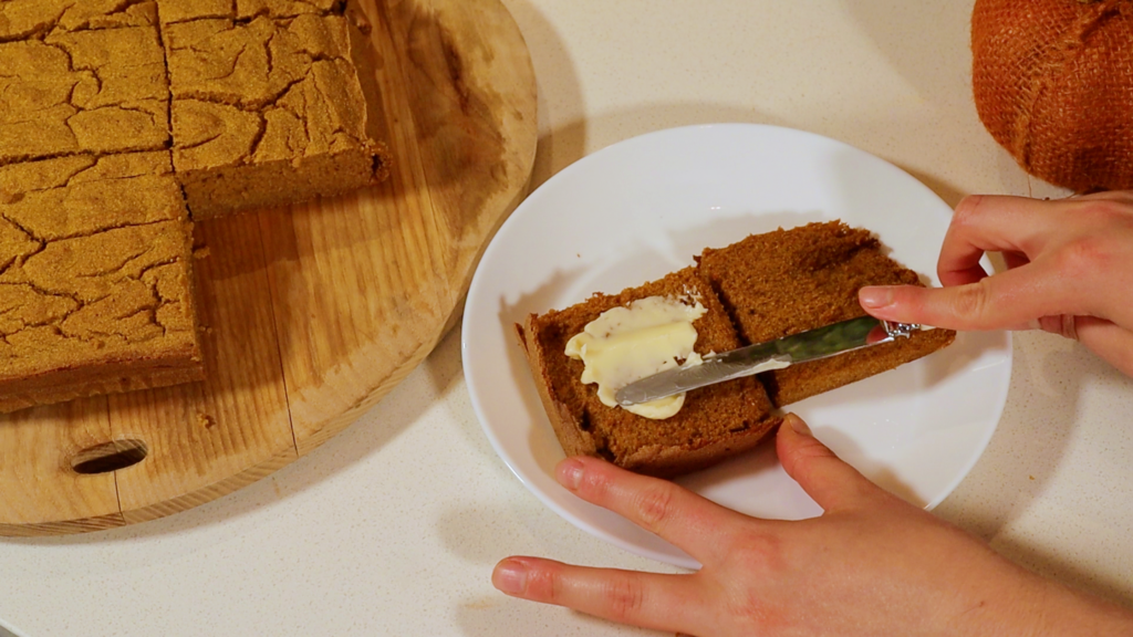 hands buttering a slice of pumpkin cornbread