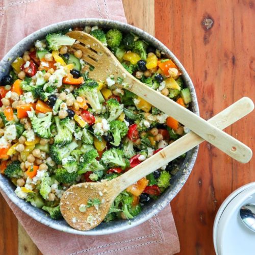 Serving bowl on a wooden table, inside the bowl is delicious feta & chickpea rainbow salad