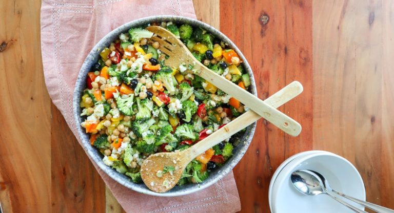 Serving bowl on a wooden table, inside the bowl is delicious feta & chickpea rainbow salad