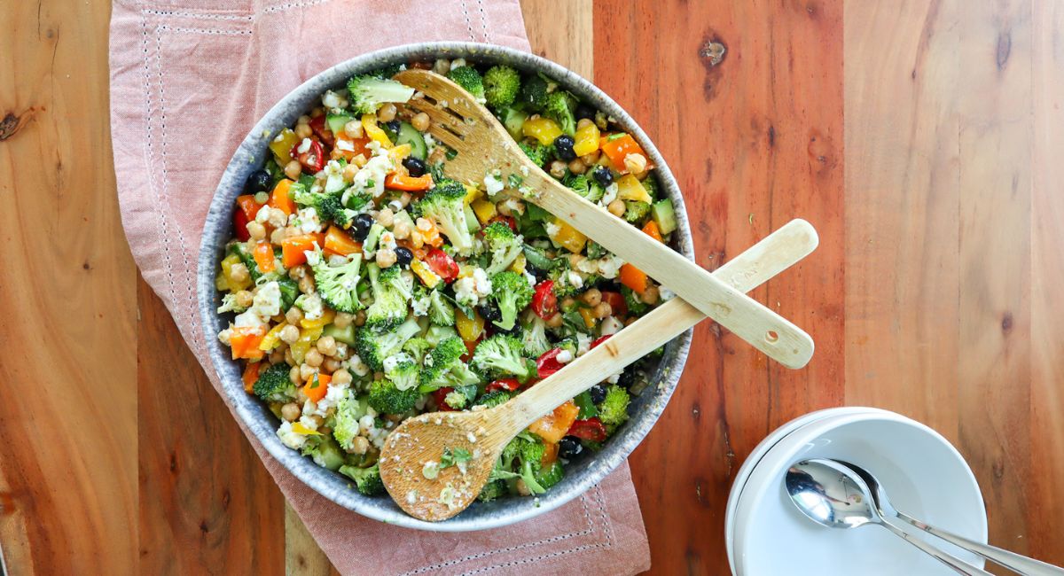 Serving bowl on a wooden table, inside the bowl is delicious feta & chickpea rainbow salad